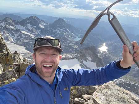 Justin on a mountain summit, holding up an ice axe